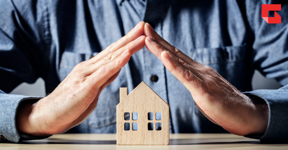 Hands protecting a small wooden house